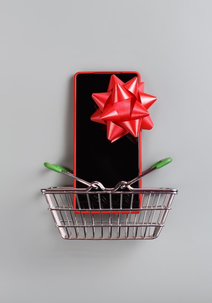 Photo smartphone,with a red bow in the toy shopping cart top view on grey