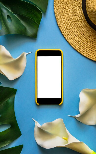 Smartphone with straw hat, tropical leaves Monstera and white callas