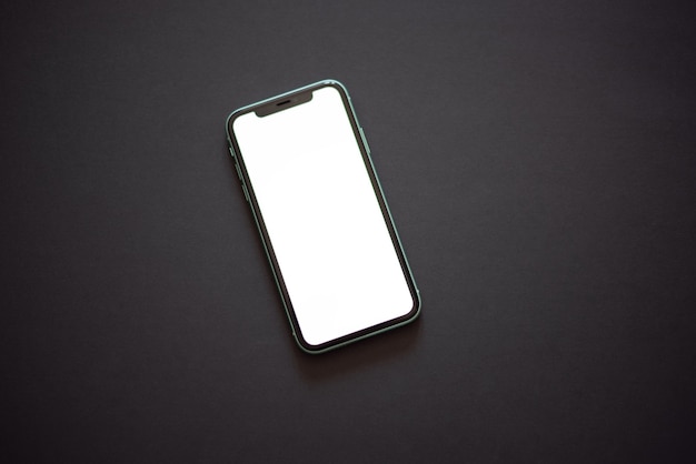 暗い背景に白い画面がオンになっているスマートフォン上面図フラットレイ
