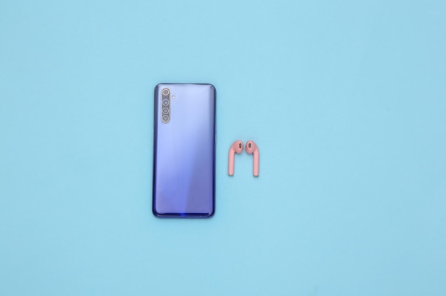 Smartphone with wireless headphones on a blue background. Top view