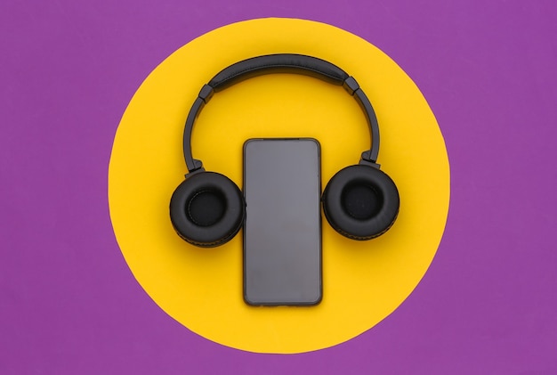 Photo smartphone with wireless stereo headphones on purple background with a yellow circle. top view