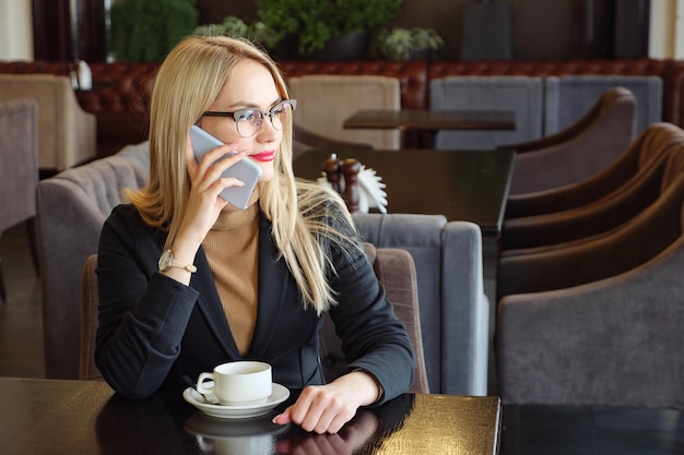 Smartphone woman talking on phone and drinking coffee in cafe, copy space