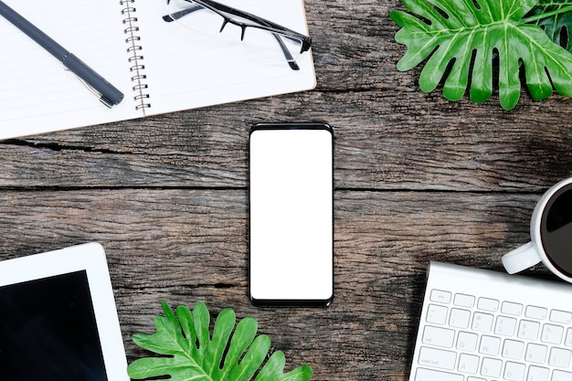 Smartphone on wooden table and supplies with keyboard and coffee