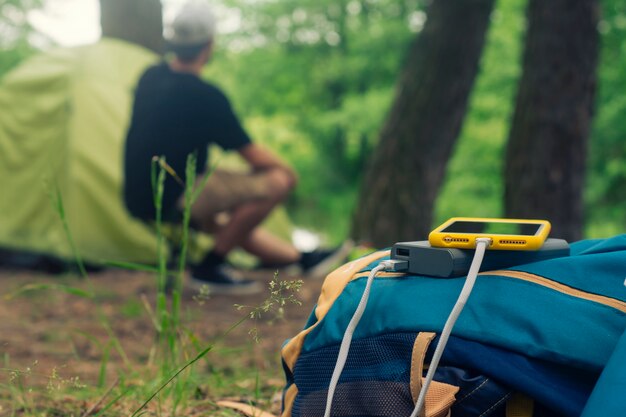 Smartphone wordt opgeladen met een draagbare oplader. Power Bank laadt de telefoon buiten op met een rugzak tegen de achtergrond van een tent en een toerist.