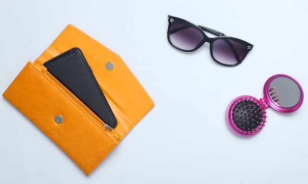 Smartphone in yellow leather wallet, sunglasses, mirror hairbrush