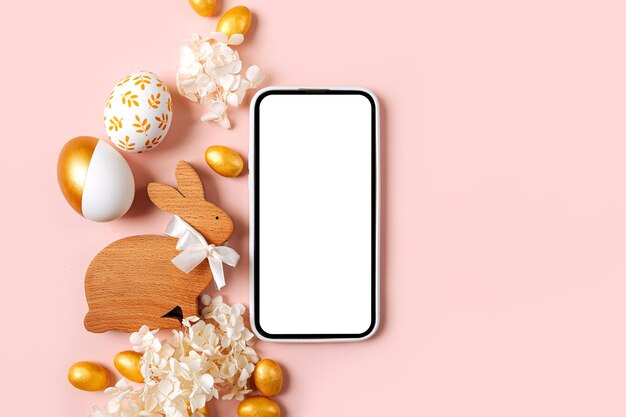 Smartphonemodel met gouden paaseierensuikergoed en bloemen op pastelroze achtergrond Vakantieconcept Vrolijk Pasen