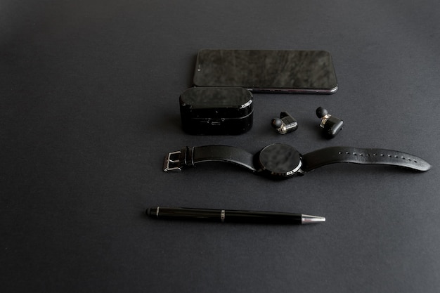 Smartwatch and phone with pen and headphones on a monochromatic background