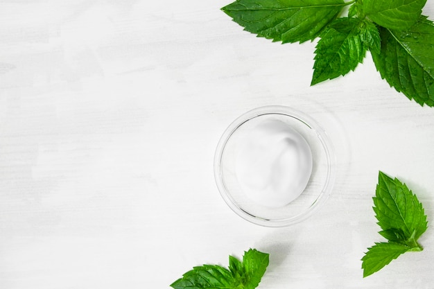 A smear of cosmetic white cream on a white wooden table with green mint leaves Organic cosmetics