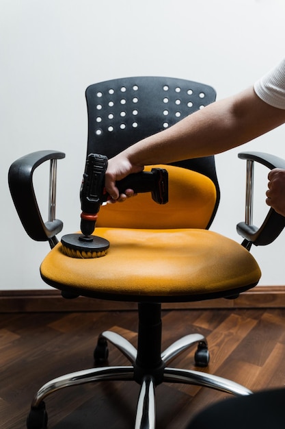 사진 드라이클리닝을 위해 드릴로 드릴을 사용하여 안락의자에 세제를 바르고 드라이클리닝을 위해 가정 내부의 의자에 세제를 바릅니다.