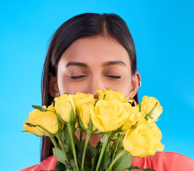 ギフトの満足感と春のためにスタジオで女性と花の花束とバラの香りを嗅ぎます自然な香りと製品のための青い背景に女性と幸せで花のプレゼントをリラックスします