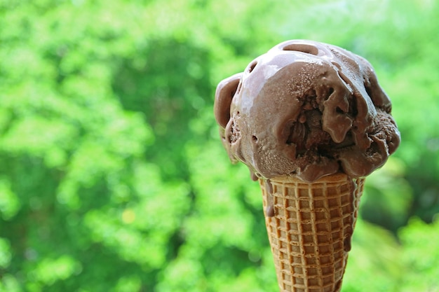 Smeltend chocolade-ijs in kegel geïsoleerd op wazige zomertuin