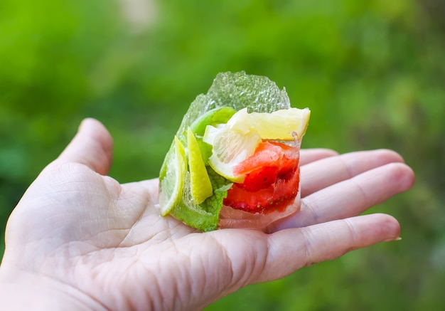Smeltend ijsblokje met aardbei, citroen en verse groene muntblaadjes in een handje