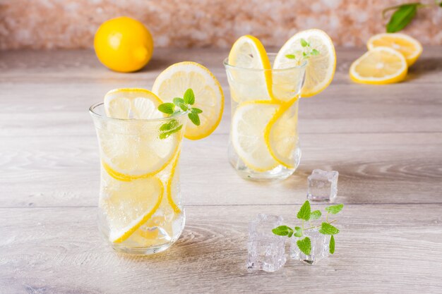 Smeltende ijsblokjes, verse muntblaadjes en water met citroen in een glas op een houten tafel