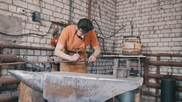 Smid buigt ijzeren staaf met hamer - metalen werkplaats, close-up, telefoto