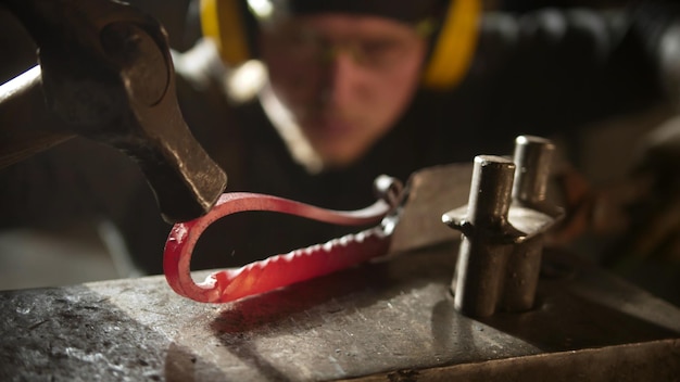 Smid smeedt een metalen handvat met een ongebruikelijk ontwerp met een hamer