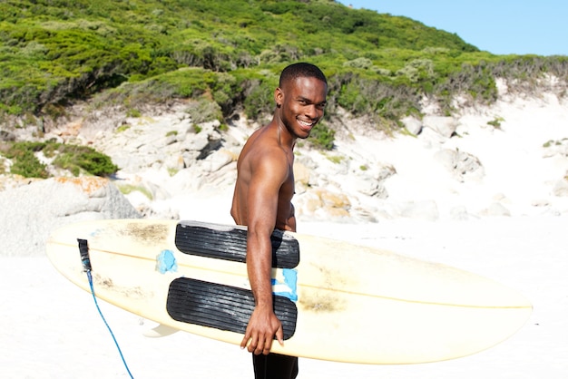 Smiing giovane uomo africano in spiaggia con tavola da surf