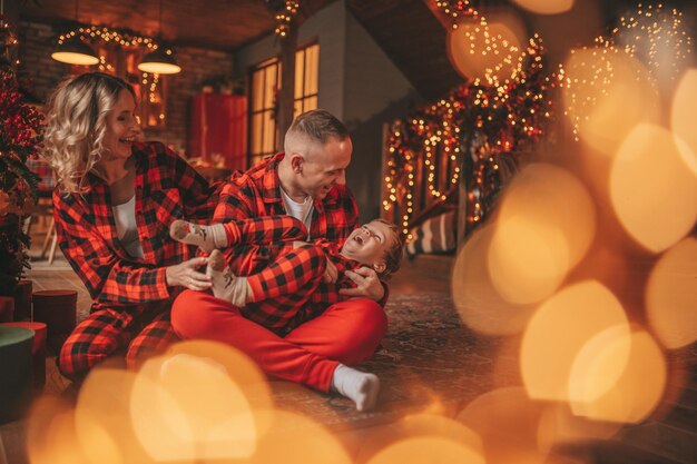 Photo smile active parents with small son in red checkered sleepwears waiting santa indoor