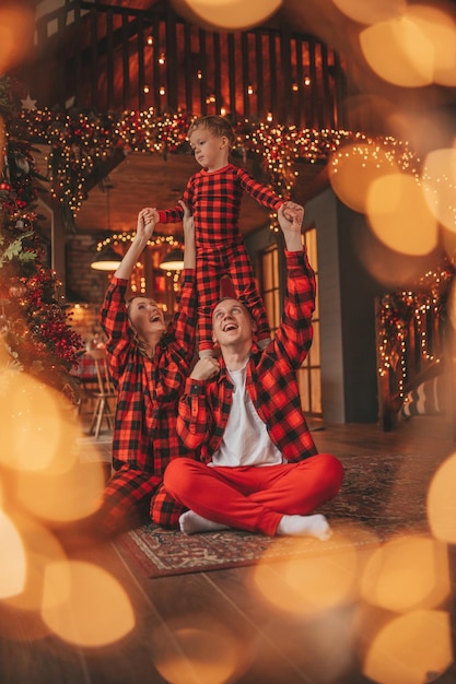 Photo smile active parents with small son in red checkered sleepwears waiting santa indoor
