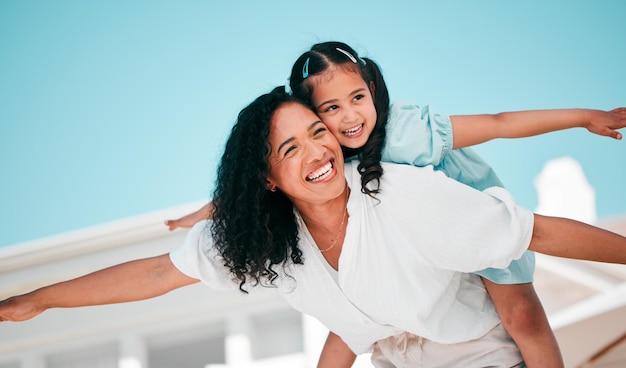 Smile airplane and mother with her child in the outdoor garden at their family home for adventure Playful happy and young mom carrying her girl kid on her back while bonding and playing together