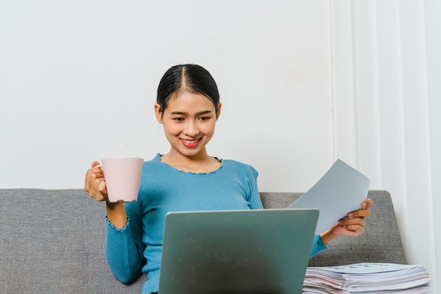 Sorridi una donna d'affari asiatica che usa il laptop mentre è seduto sul divano a casa