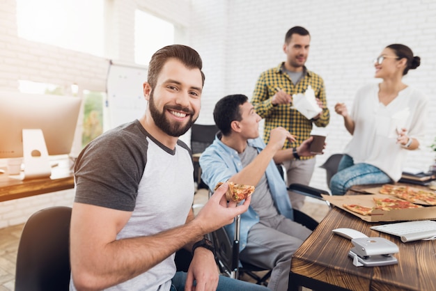 笑顔のひげを生やした男はオフィスでピザを食べています。