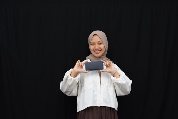 Smile beautiful asian girl in hijab, showing blank mobile phone horizontal screen