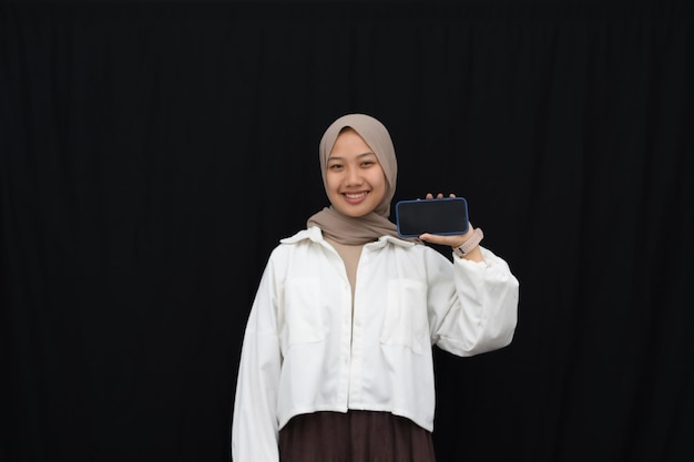 Photo smile beautiful asian girl in hijab, showing blank mobile phone horizontal screen