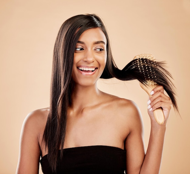 Smile beauty and a woman brushing her hair in studio on a cream background for natural or luxury style Haircare face and shampoo with a happy young indian female model at the salon or hairdresser