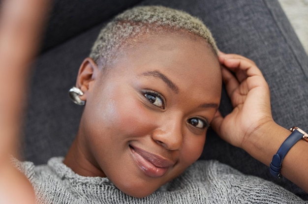 Smile black woman on sofa and phone selfie taking a profile picture for social media or online dating app Relax happy and woman laying on living room couch taking photo for self love from above