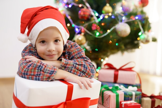 The smile boy sit with a gift box near the christmas tree