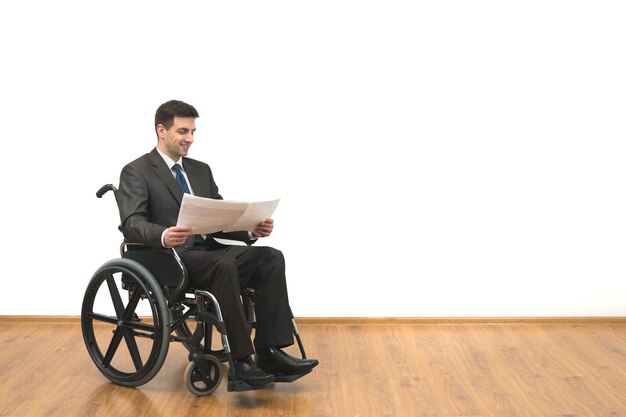 The smile businessman in a wheelchair holding papers on the white wall background