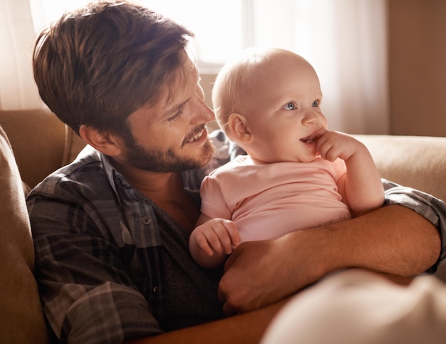 Smile dad and hug baby on sofa in home living room playing or bonding together Happiness care and father embrace infant newborn or child on couch in lounge having fun and enjoying quality time