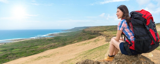 smile elegant climber sitting on the hills to resting and enjoying watch coast landscape with carrying baggage backpack on vacation with banner crop for copy space.