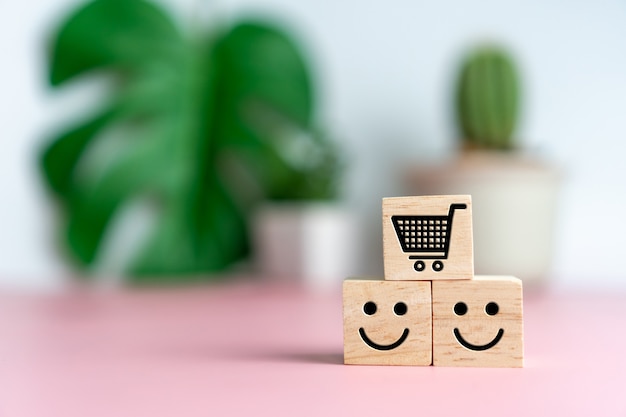 ウッドキューブの笑顔の顔とカートアイコン。楽観的な人、またはショッピングの際のサービス評価と満足度の概念。