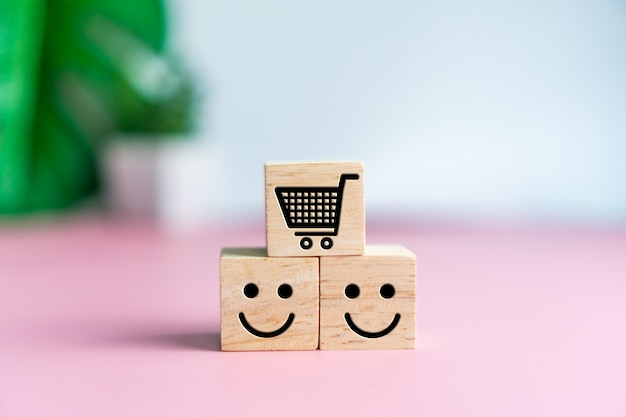 Photo smile face and cart icon on wood cube. optimistic person or people feeling inside and service rating when shopping, satisfaction concept.