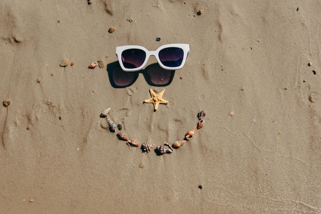 Smile face drawn on sand with shells and sunglasses