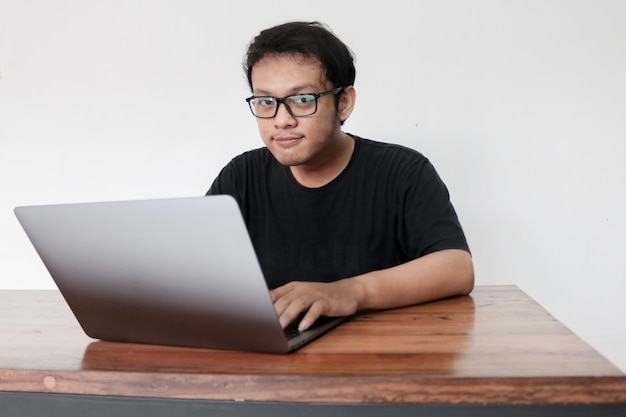 Smile face and Funny tricky awkward smirk face of Young Asian man with hand in chin in a black tshirt in a front of a laptop