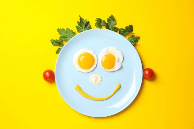 Фото Улыбающееся лицо из тарелки с яичницей на желтом фоне, вид сверху