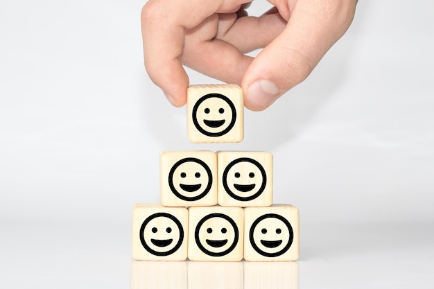 Улыбающееся лицо на деревянном кубе, люди, чувствующие себя внутри, и концепция удовлетворенности рейтингом обслуживания в бизнесе