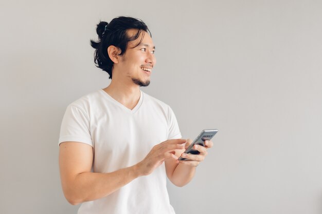 白のカジュアルなtシャツを着た笑顔と幸せの長い髪の男がスマートフォンを使用しています。