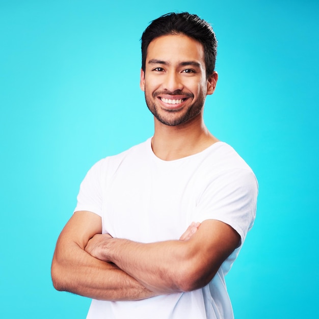 Smile happy and portrait of Asian man arms crossed with casual fashion isolated in a studio blue background Relax calm and young male person proud or confident mindset natural and happiness