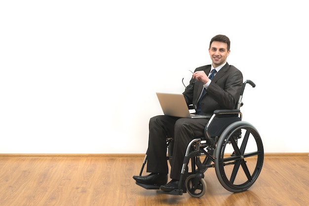 The smile man in a wheelchair sitting with a laptop on a white wall background