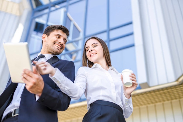 The smile man and woman stand with a tablet on the background of the building