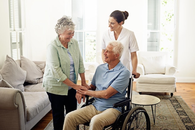 Smile old man in wheelchair with wife and nurse at nursing home for disability help and rehabilitation Healthcare disability and happy senior couple with caregiver in living room for elderly care