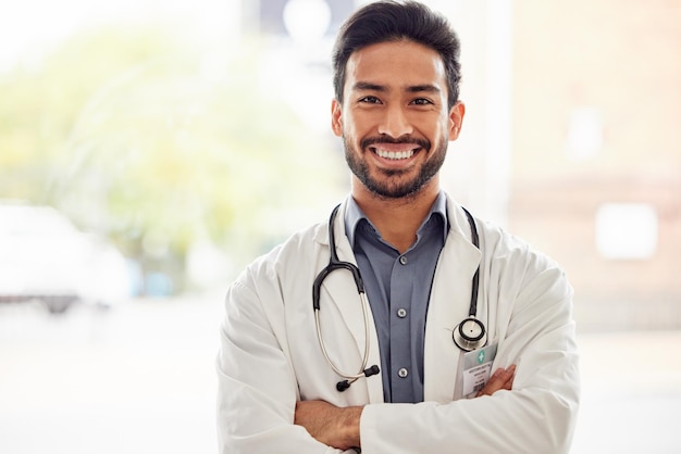 Smile portrait and asian man doctor with arms crossed in hospital for consulting exam and help on blurred background Happy face and guy healthcare expert proud of service while working at clinic