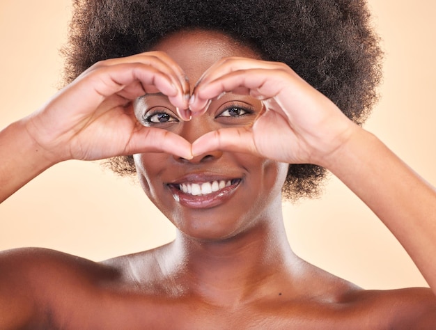 Smile portrait and a black woman with heart hands on a studio background for love or support Happy emoji and face of African girl or model with a sign or gesture for care or kindness on a backdrop