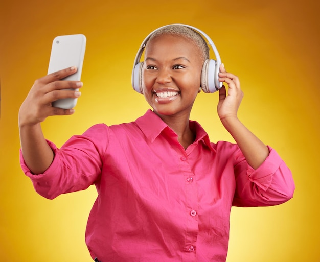 Smile selfie and black woman with headphones for music radio and podcast in studio isolated on a yellow background profile picture photographer and african person or influencer on social media