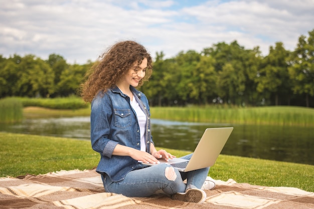 La donna sorridente con un laptop si siede sull'erba