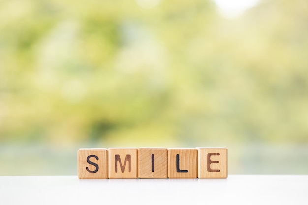 Smile word is written on wooden cubes on a green summer background Closeup of wooden elements