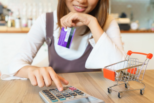 Smiled woman pushing calculator and holding credit card 